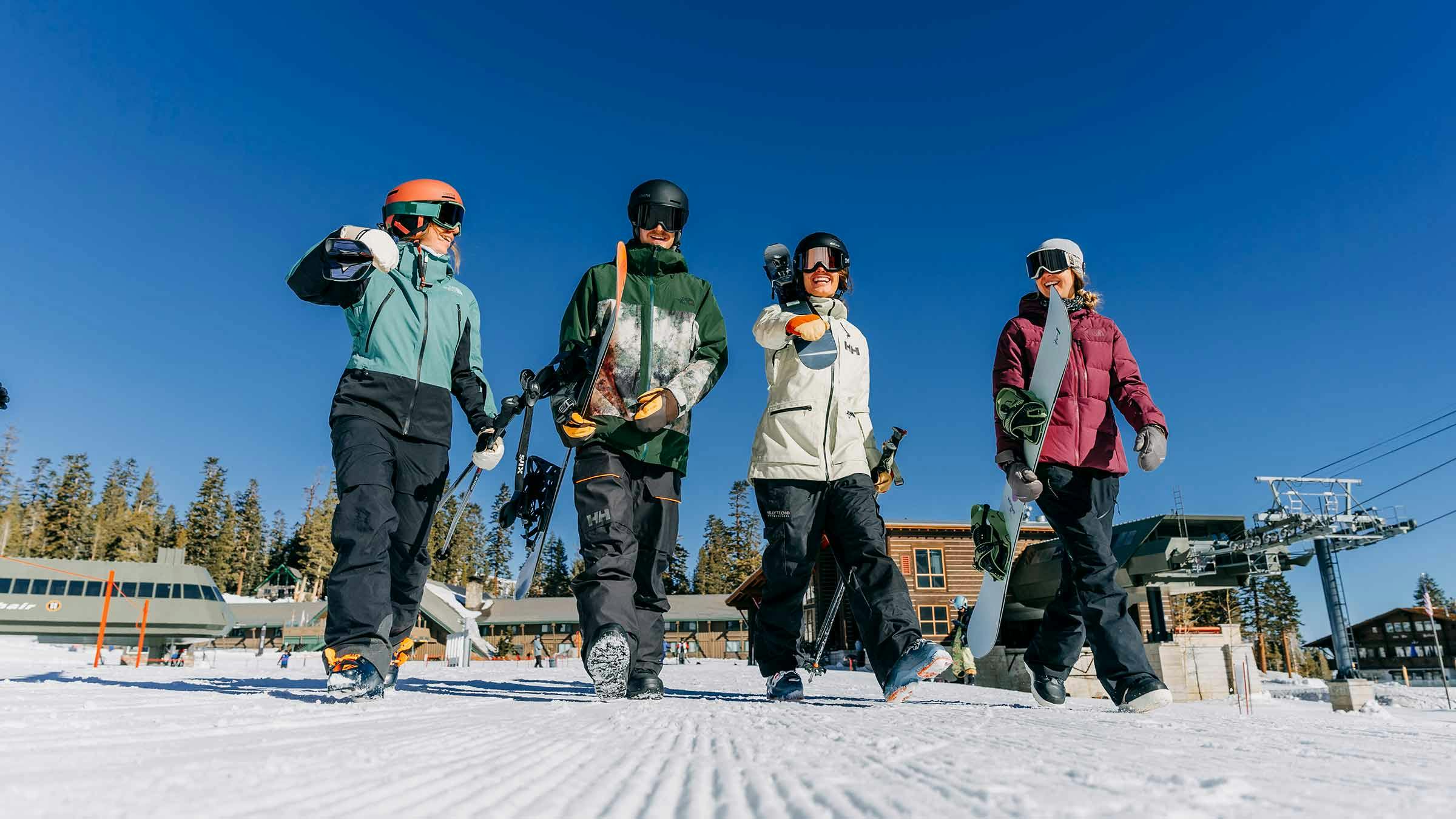 Friends walking on snow carrying their ski and snowboard gear at Mammoth Mountain.